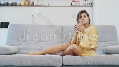 穿着浴袍的年轻女子坐在沙发上的房间里。 他坐在沙发上喝咖啡看电视。 舒适